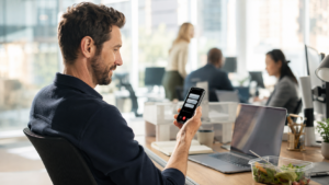 Professional with hearing loss reading real-time captions of a phone call on his smartphone at his office desk